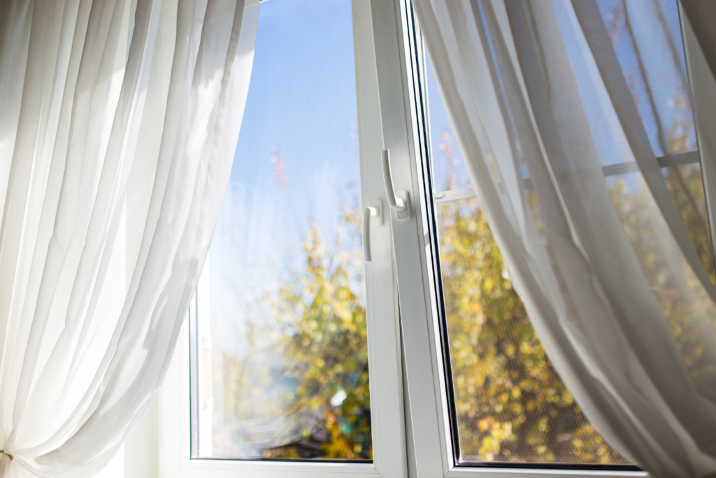 a photograph of a white window frame with white curtains and tilt and turn windows