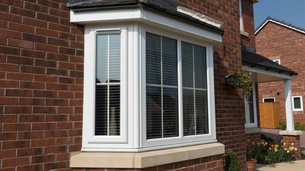 a photograph of a red brick house with a 4 part bay window in stone and white uPVC