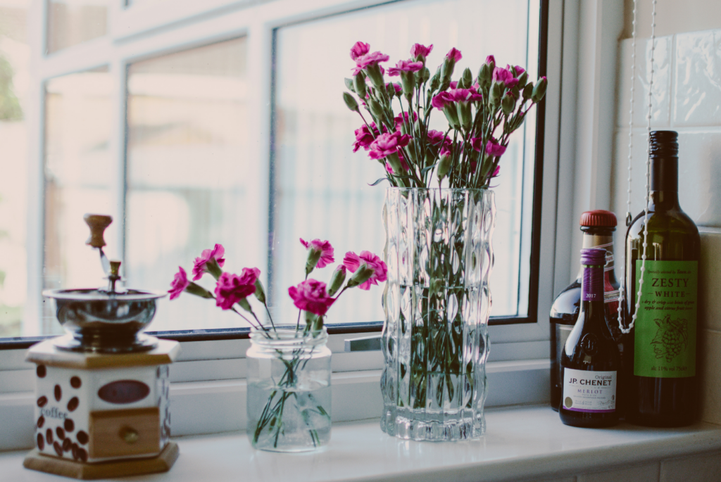 a photograph of a white window with wine, flowers in a vase and a coffee grinder on the windowsill