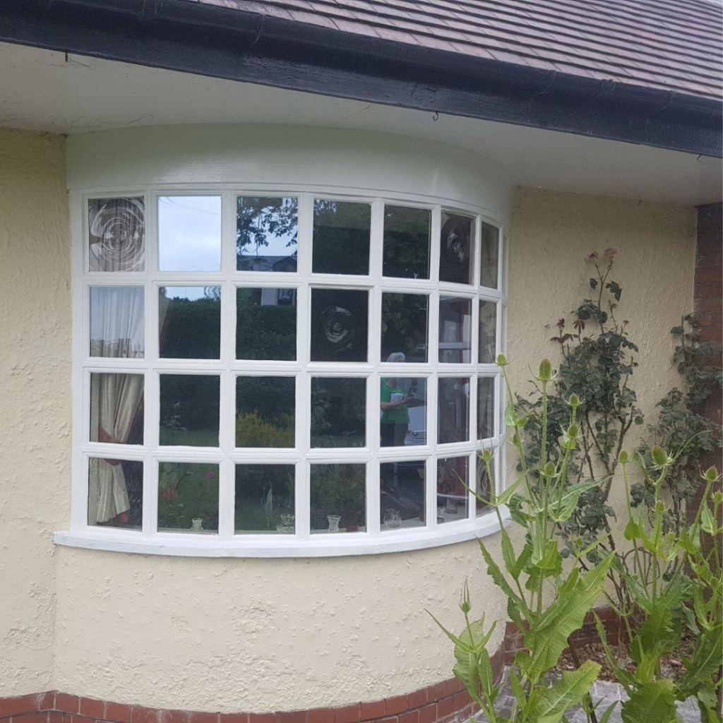 A photograph of a house with cream rendering and a white bow-shaped window with bullseye decorative glass