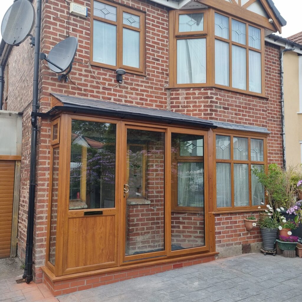 A photograph of a red brick house with golden oak windows and a golden oak upvc porch with slate tiled roof